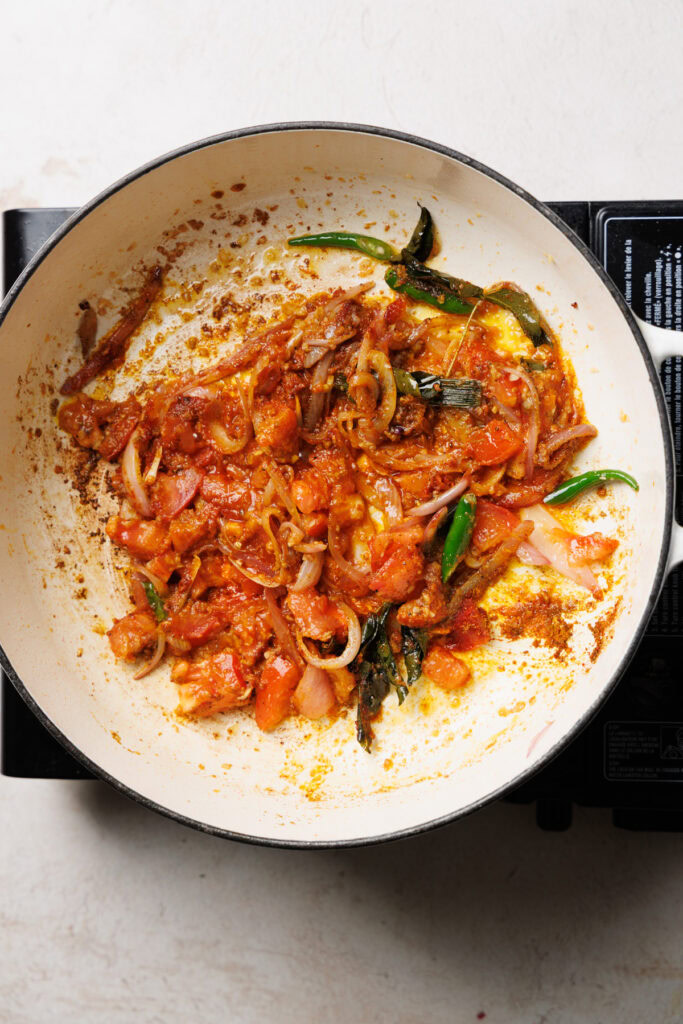 cooking the spices along with tomatoes in a pan.