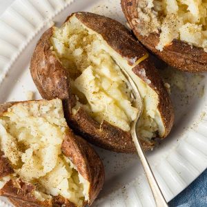 air fryer baked potatoes with butter and a fork on a plate.