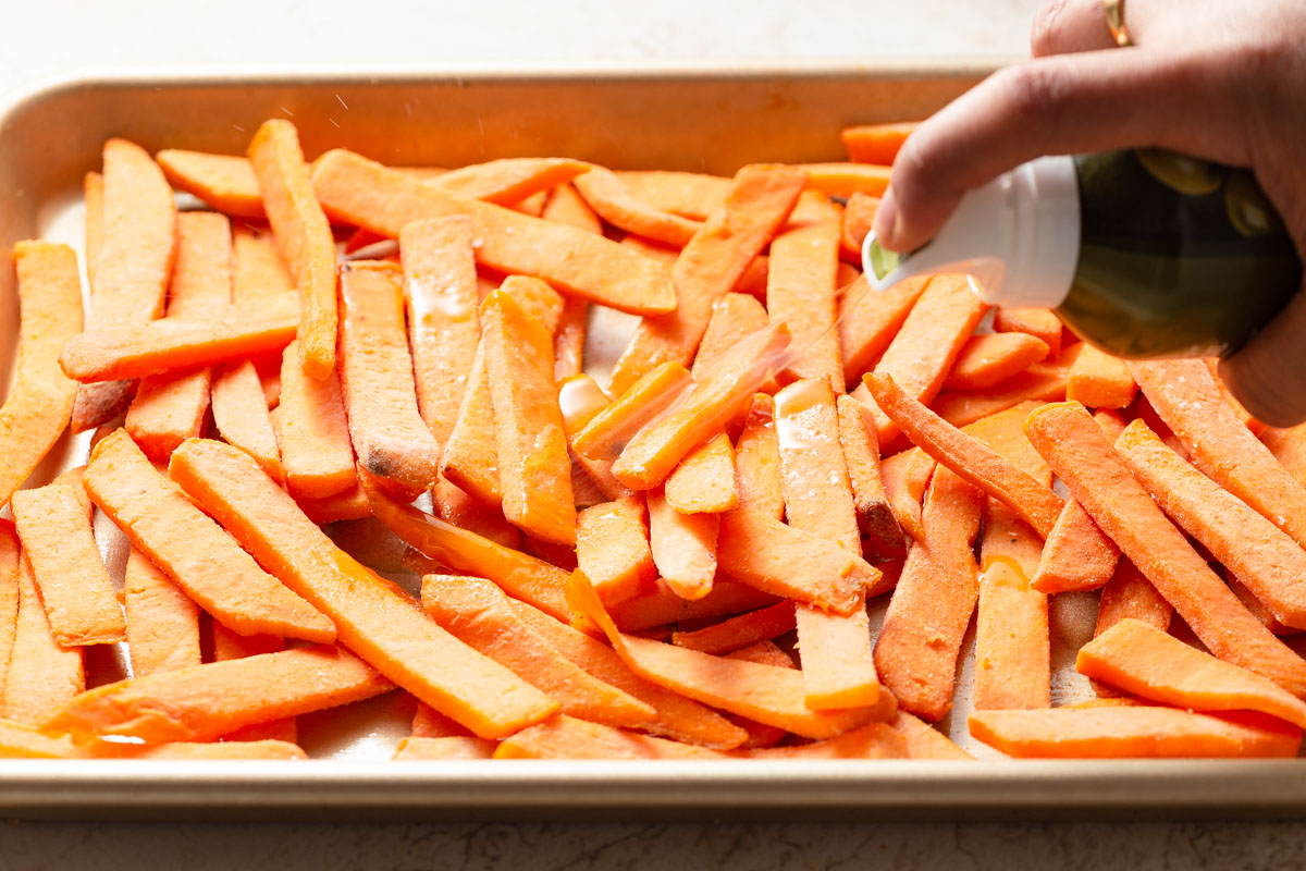 spraying the frozen sweet potato fries with an oil mister.