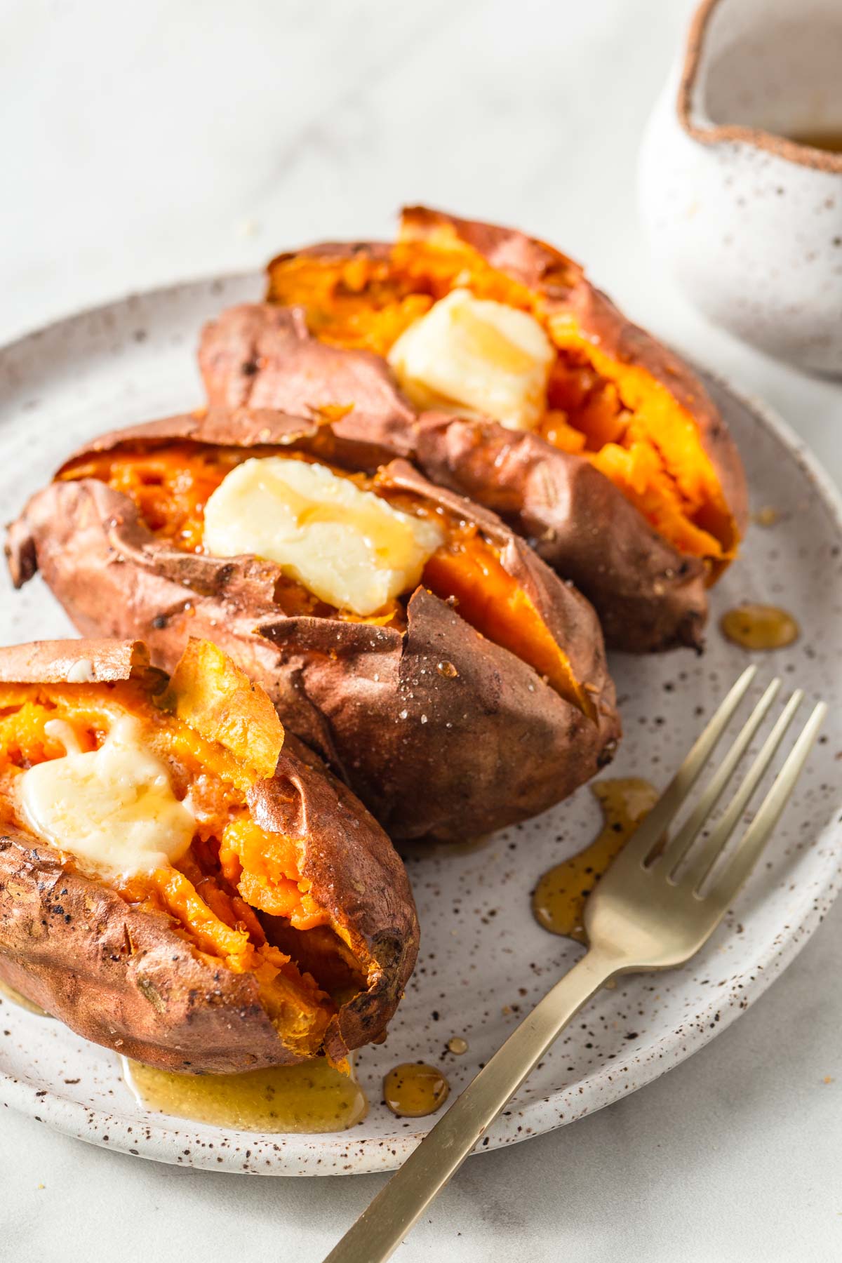 air fryer baked sweet potatoes on  a plate with butter and maple syrup.