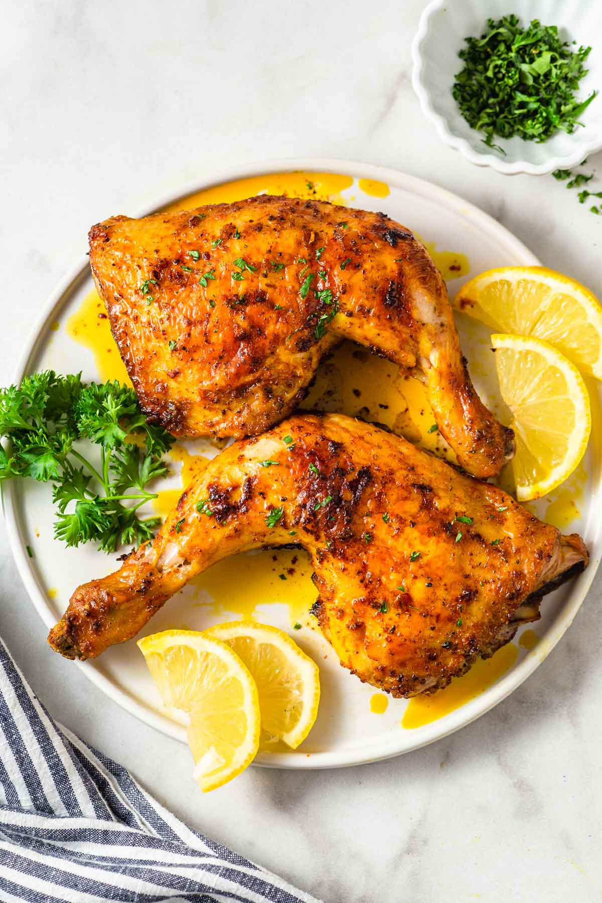 air fryer chicken leg quarters on a plate with parsley and lemon wedges on the side.