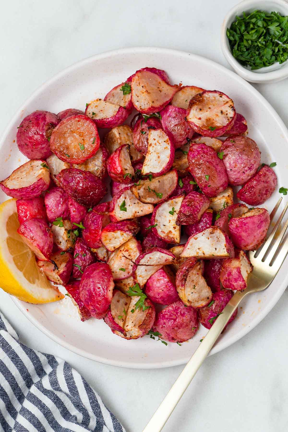 air fryer roasted radishes on a plate with parsley and lemon wedge.