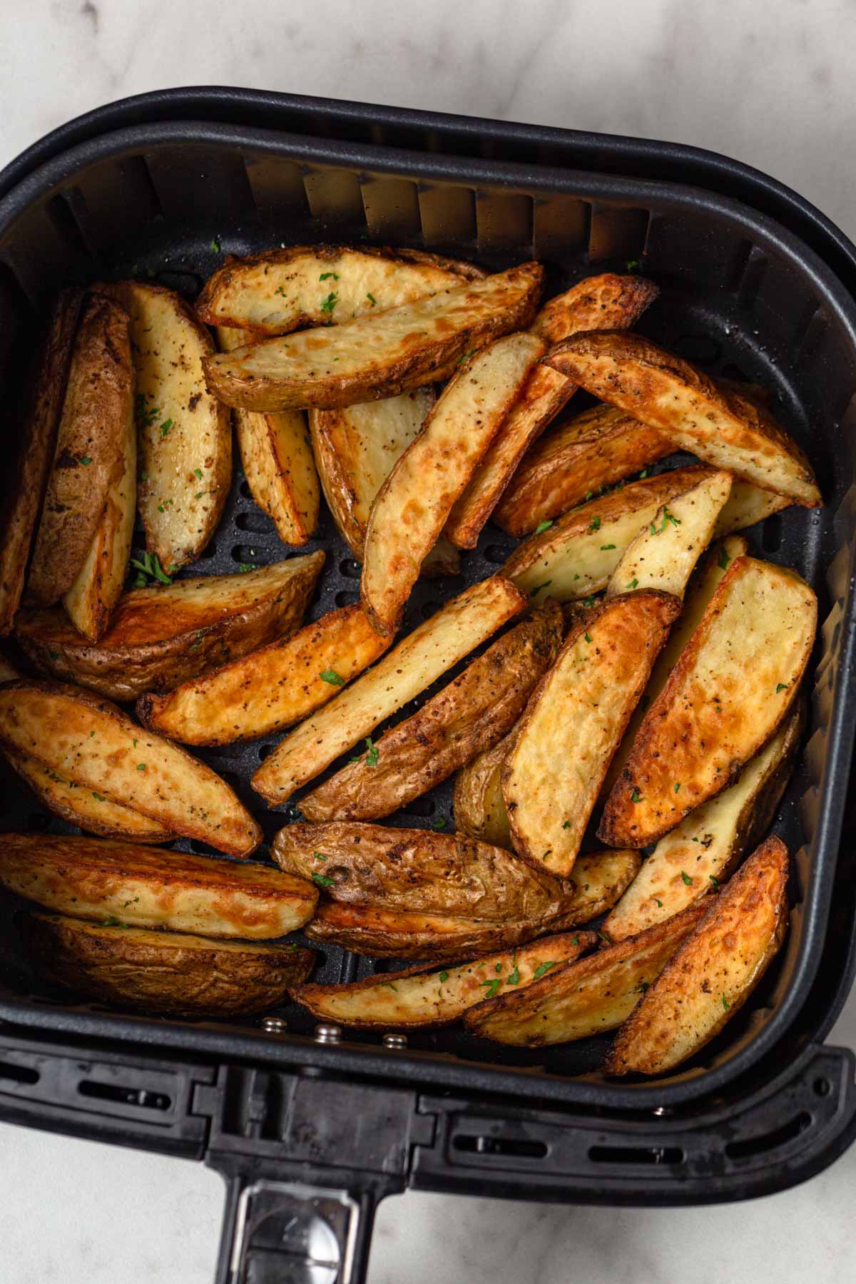 air fried potato wedges in the air fryer basket.