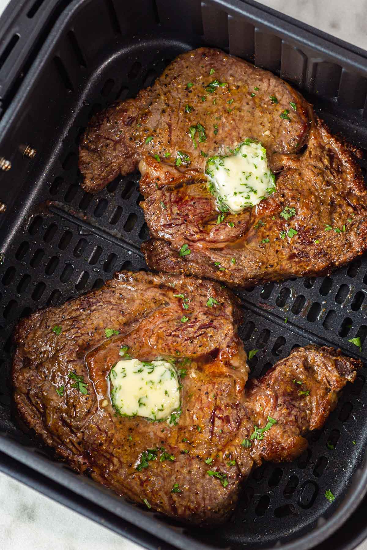 rib eye steak in air fryer with butter on top.