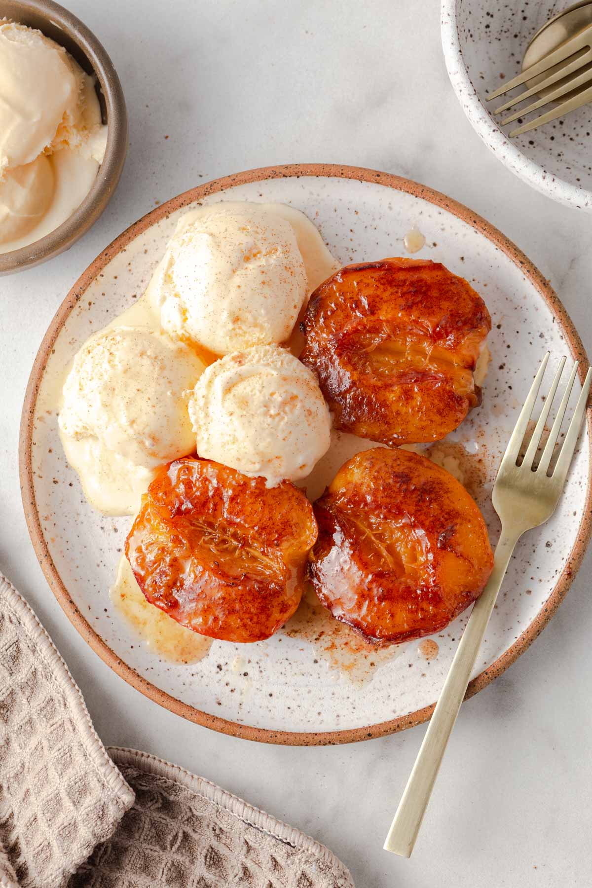 air fryer grilled peaches on a plate with ice cream and a fork.