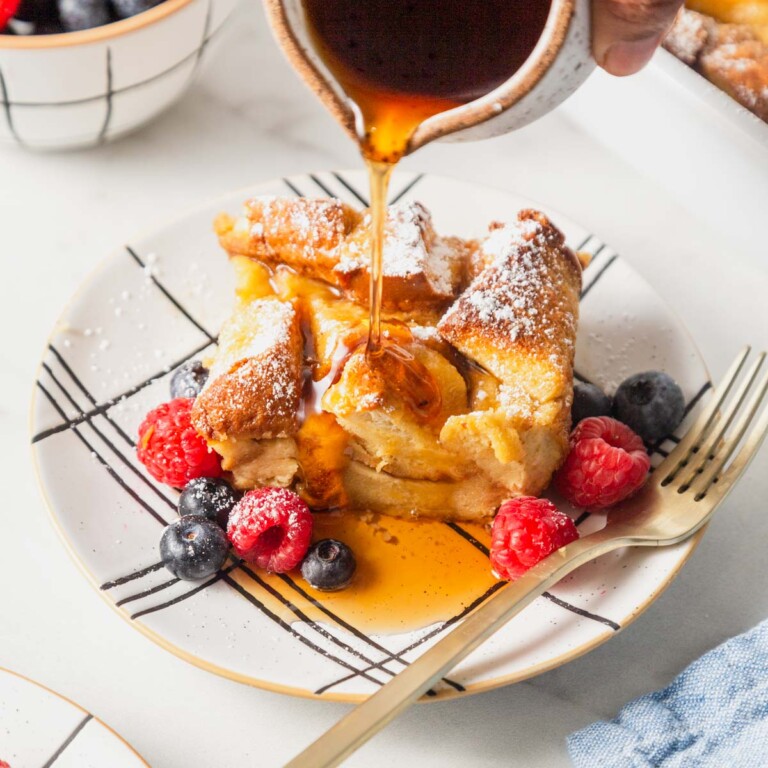 french toast casserole with berries and maple syrup poured over it.