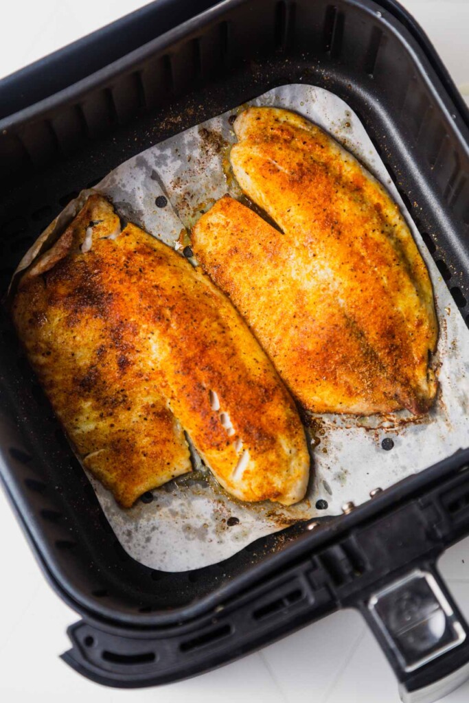 tilapia fillets seasoned with spices in the air fryer basket.