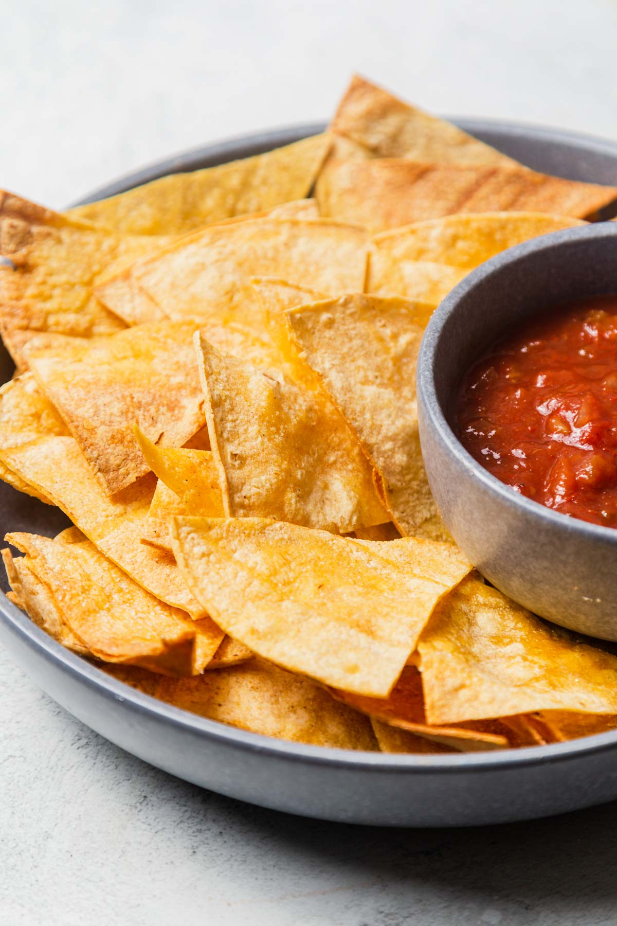 close up of air fried tortilla chips on a silver plate with salsa.