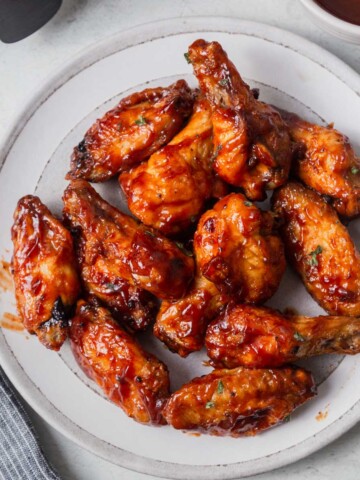 air fried bbq chicken wings on a white plate with bbq sauce on the side.