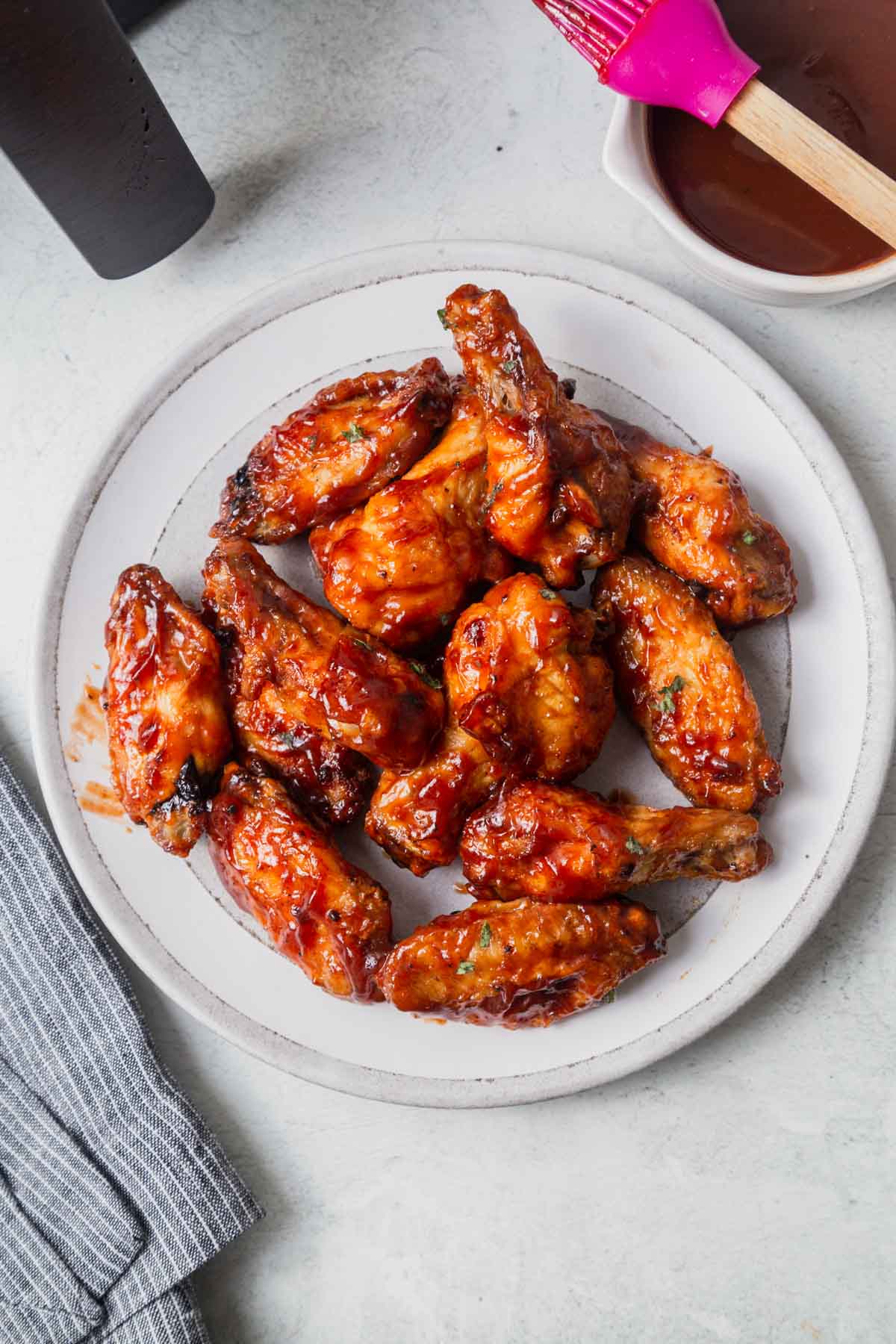 air fried chicekn wings tossed in bbq sauce on a white plate.
