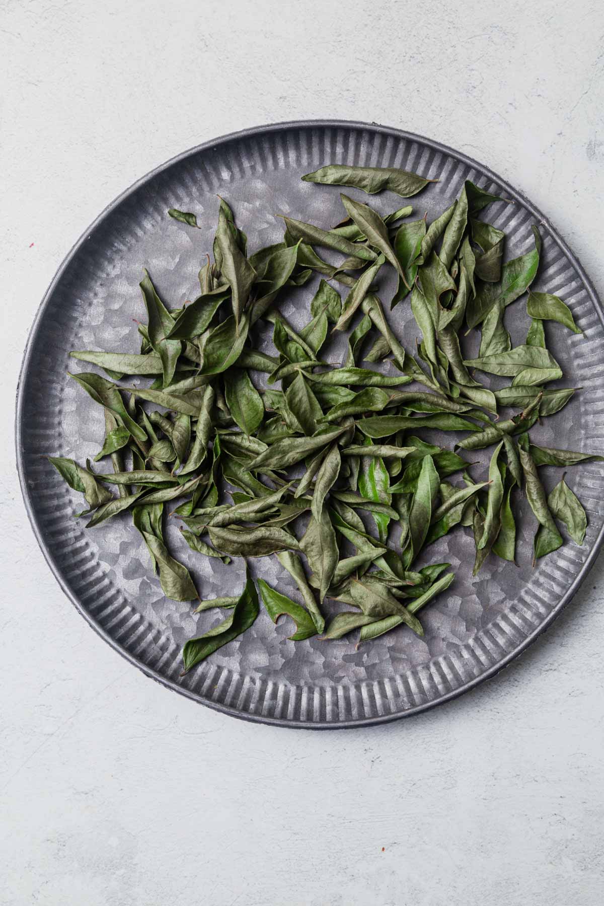 dried curry leaves on a grey tray.