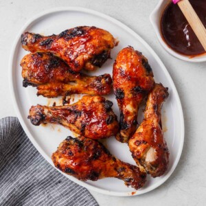 air fryer bbq chicken legs on a plate with bbq sauce on the side.