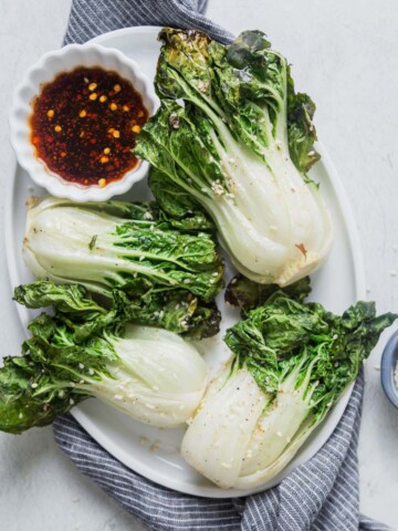 air fryer bok choy on an oval plate with dipping sauce.