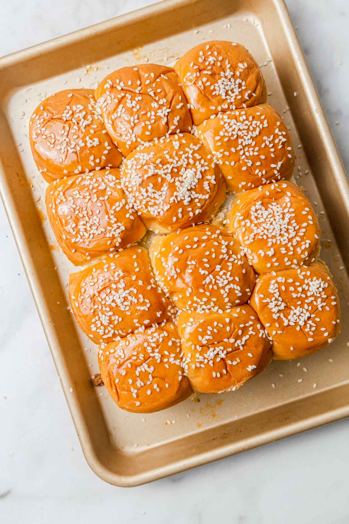 Hawaiian rolls with sesame seeds on top on a baking sheet ready for the oven.