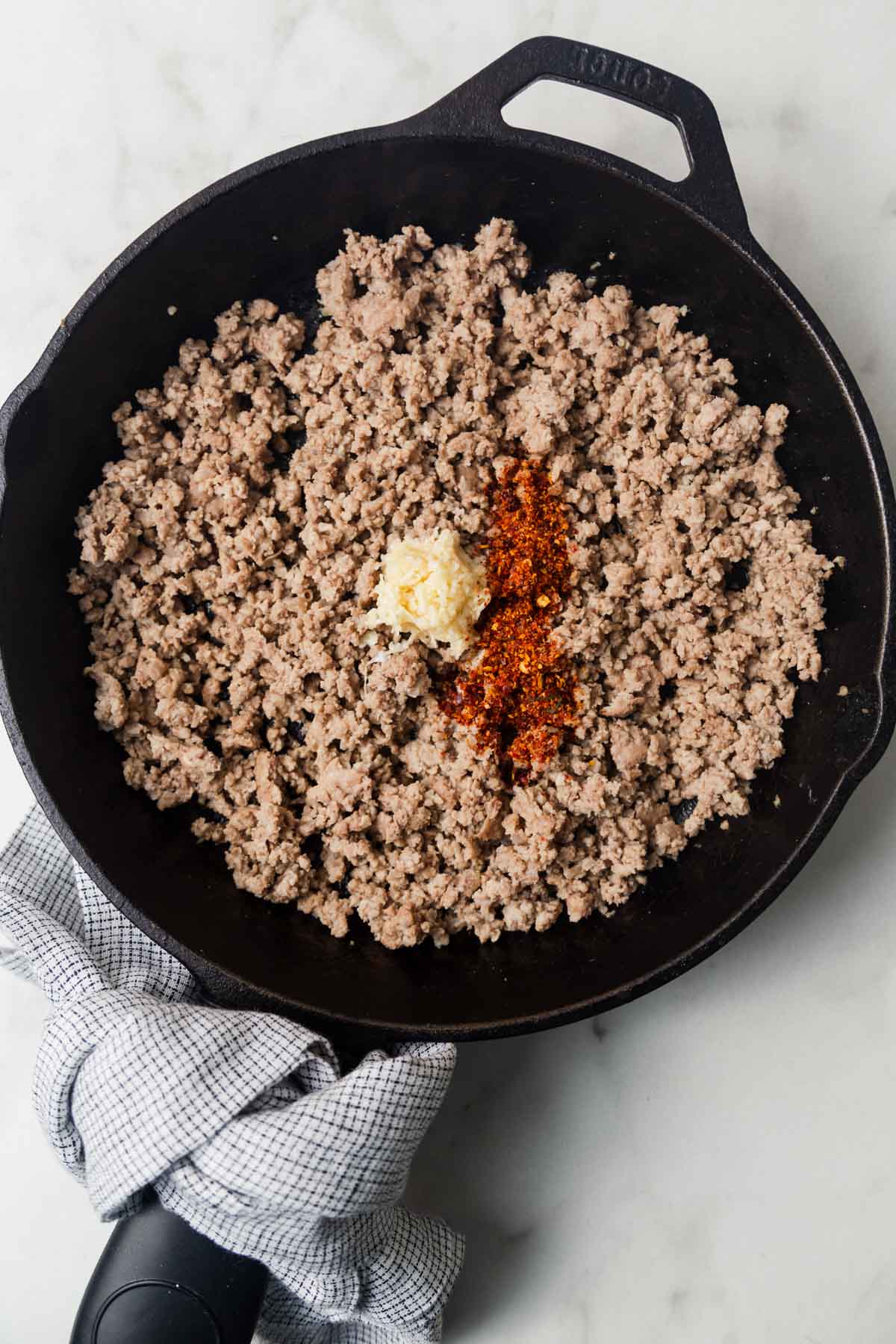 Cooked ground beef in a skillet with minced garlic and chili flakes.