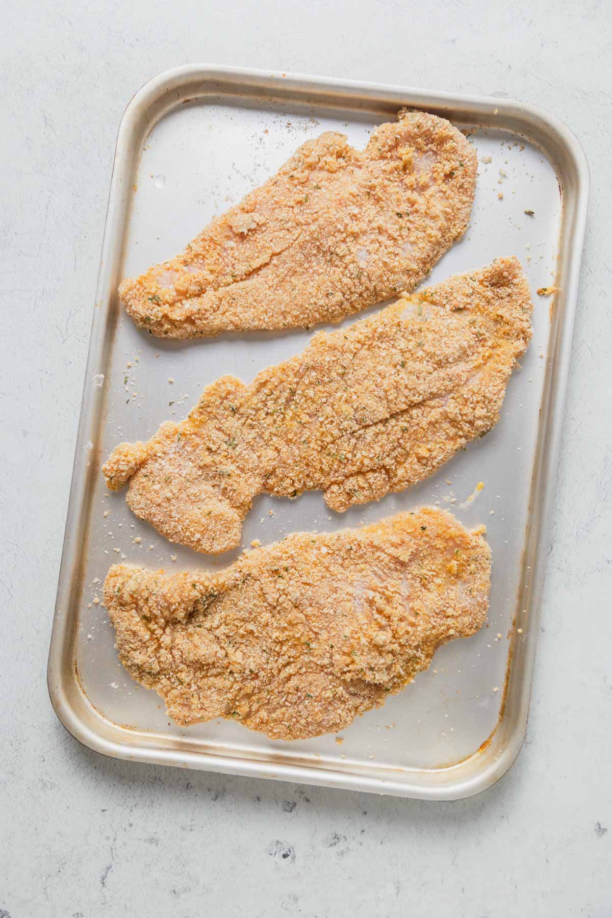 breaded chicken slices on a baking tray.
