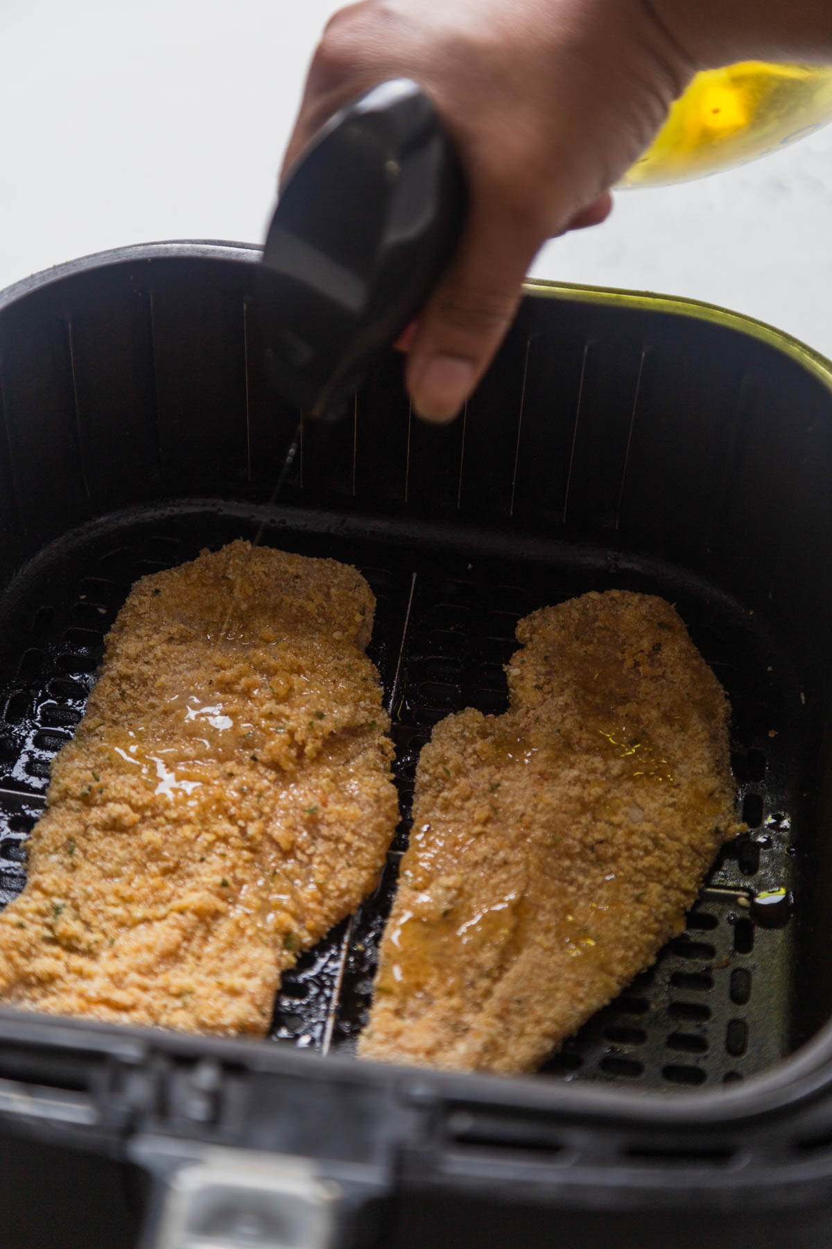spraying oil on the breaded chicken cutlets.