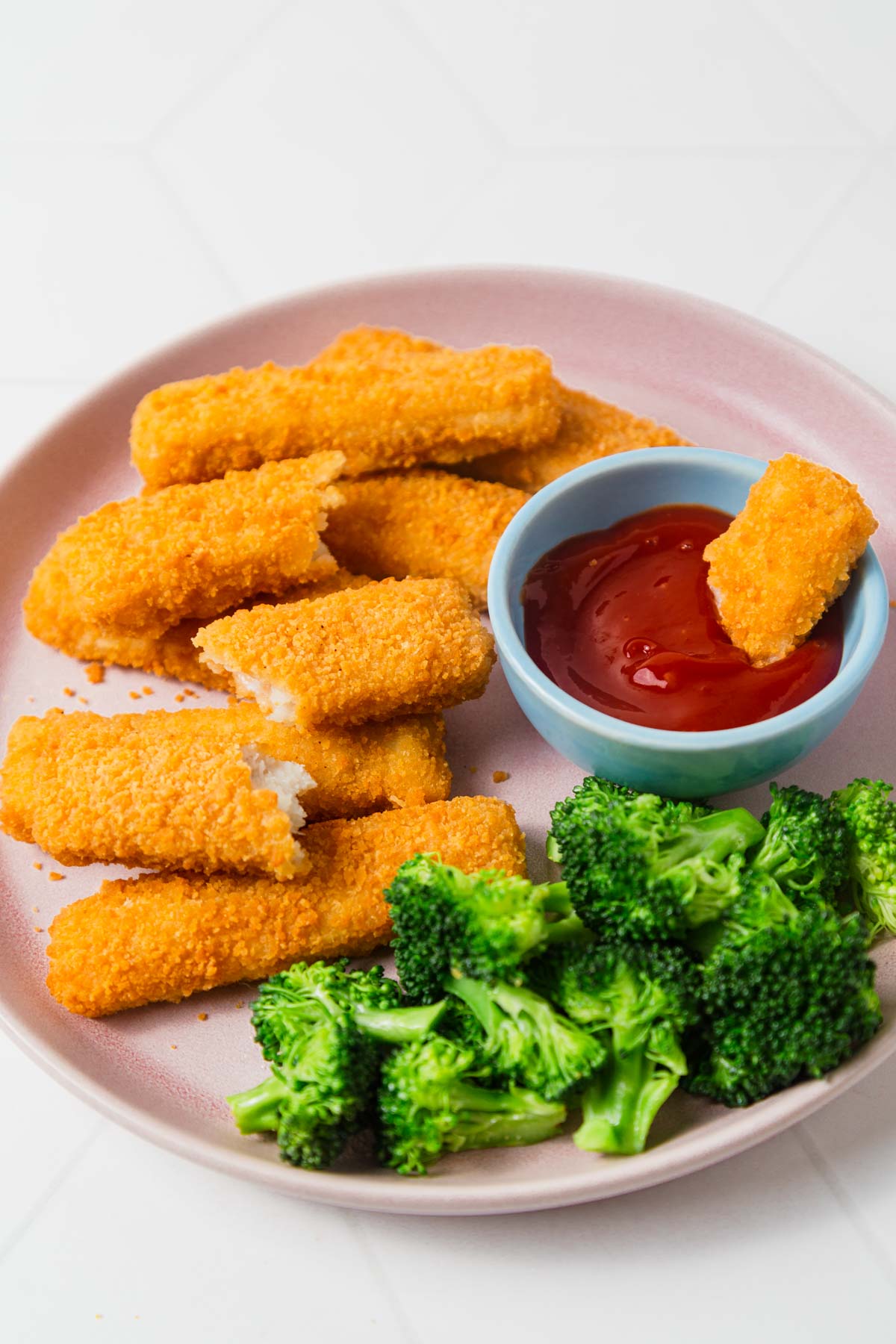 air fryer frozen fish sticks with broccoli and ketchup on a plate.