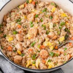 shrimp and chicken fried rice in a skillet with a spoon and green onions.