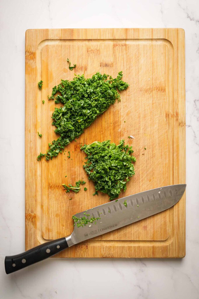 kale being chopped on a chopping board with a knife.