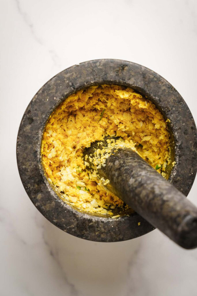 pounding the coconut with spices on a mortar.