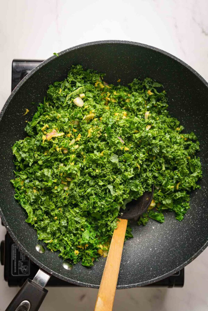 adding kale to the pan with a spoon.