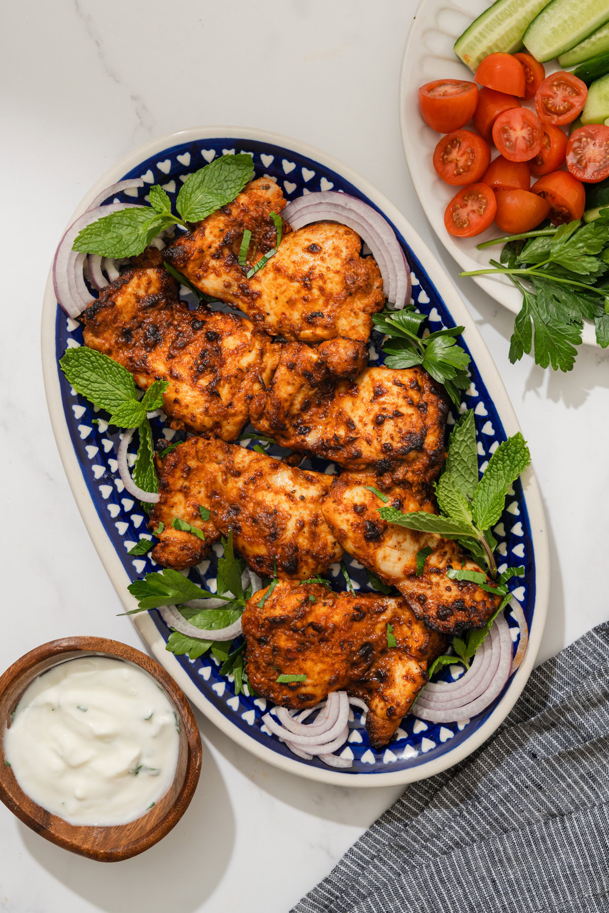 air fryer harissa chicken on a platter with yogurt sauce next to it.