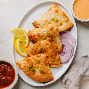 air fryer chicken quesadillas on a platter with lemon wedges and sliced onions.