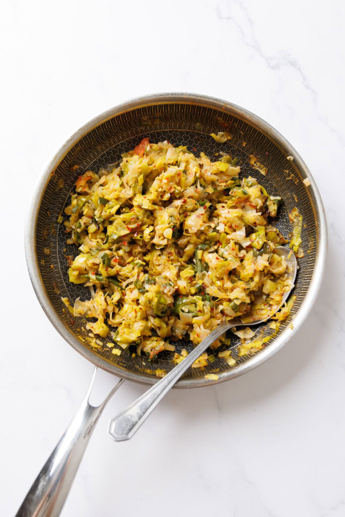 Cooked Sri Lankan leeks curry in a patterned bowl with a spoon on a white background.
