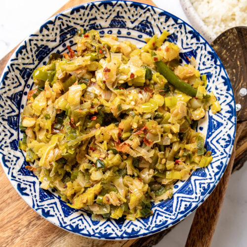 Sri Lankan leeks curry in a blue patterned bowl with a bowl of rice in the background.