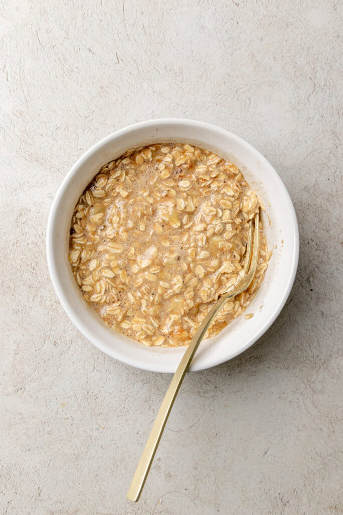 Rolled oats mixed with mashed banana in a white bowl on a light stone-textured countertop.