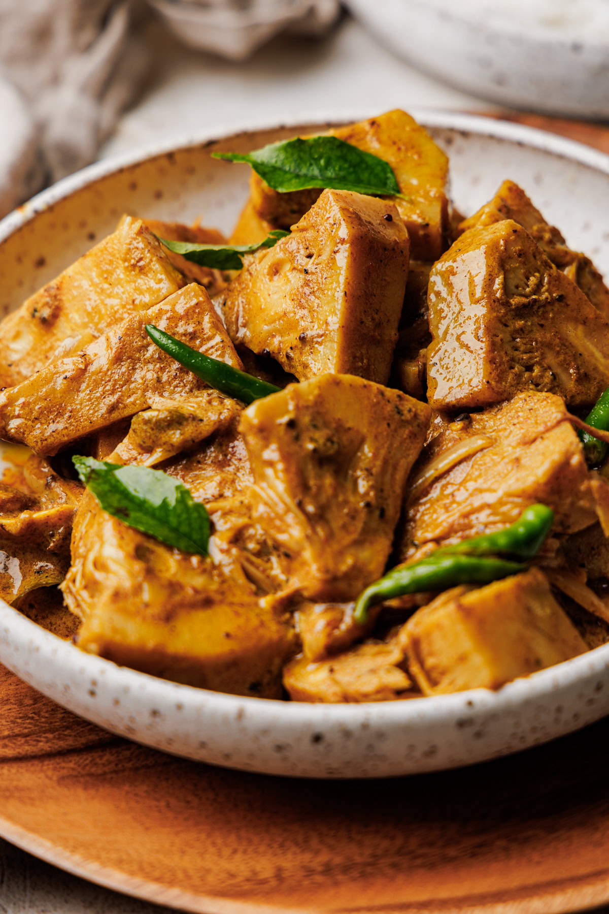 Sri Lankan jackfruit curry served in a speckled bowl with curry leaves and sliced chilies as garnish.